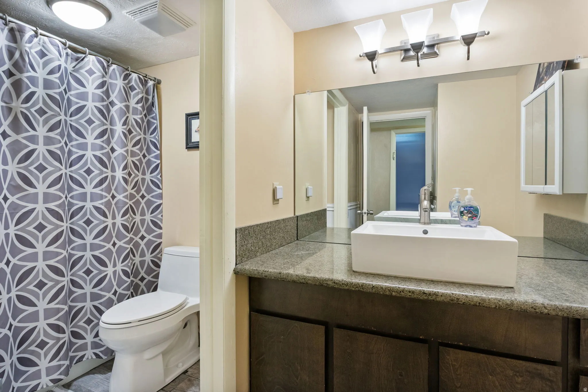 Modern bathroom featuring a rectangular vessel sink, granite countertop, wood-finish vanity, and full-width mirror