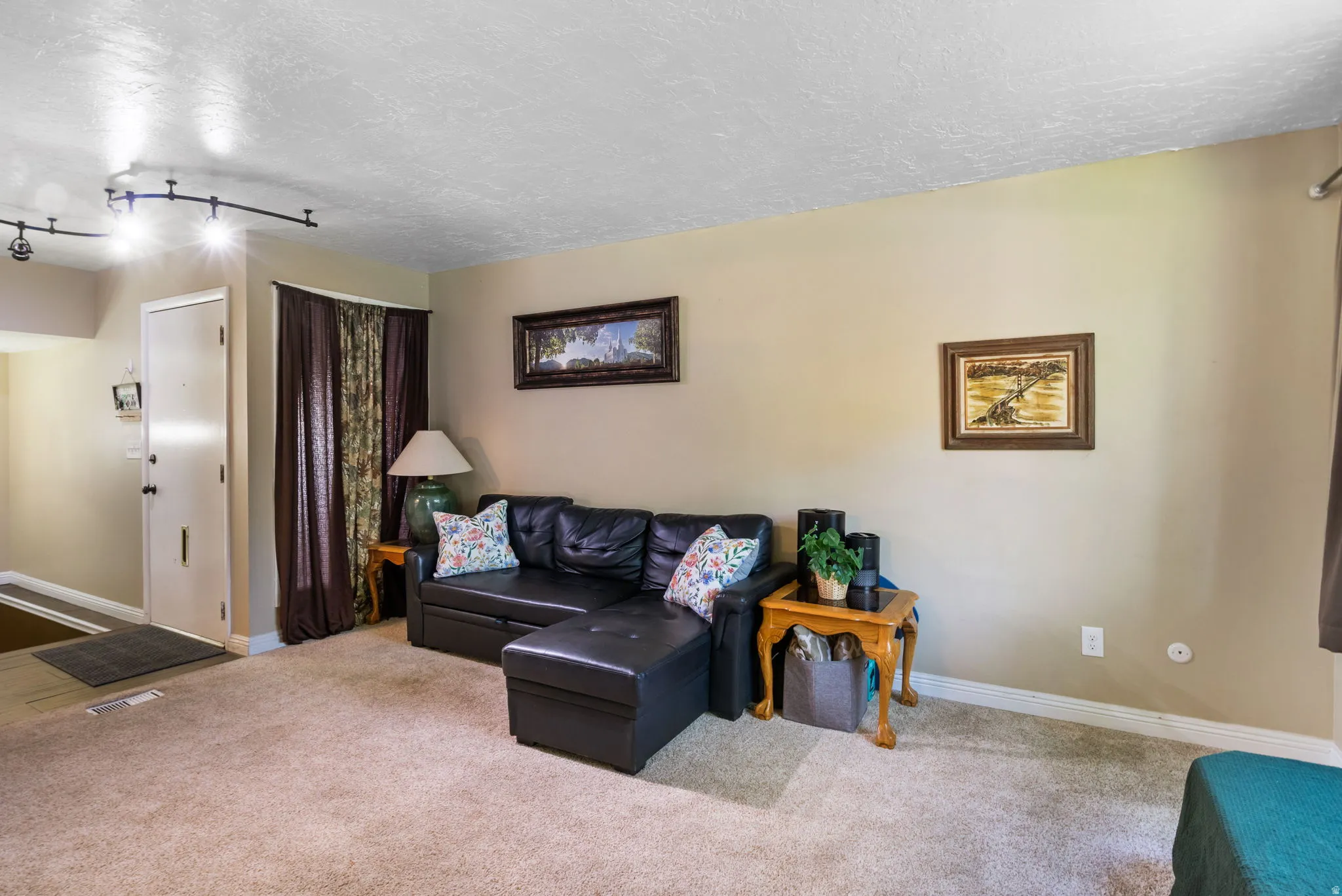 Carpeted living area featuring track lighting, a neutral wall color, and a white entry door with dark hardware