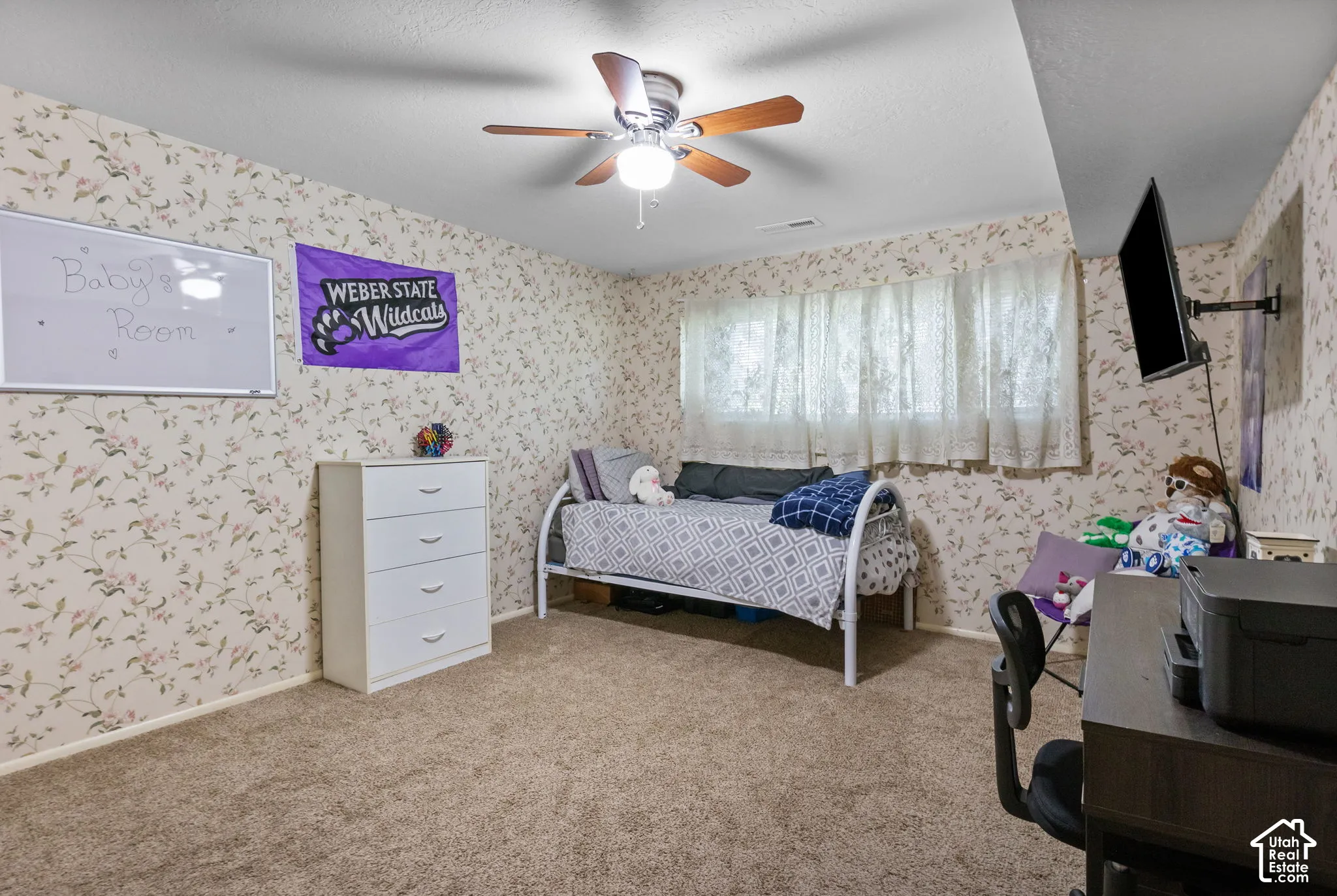 Carpeted room featuring patterned wallpaper, a ceiling fan with light fixture, and window with sheer curtains