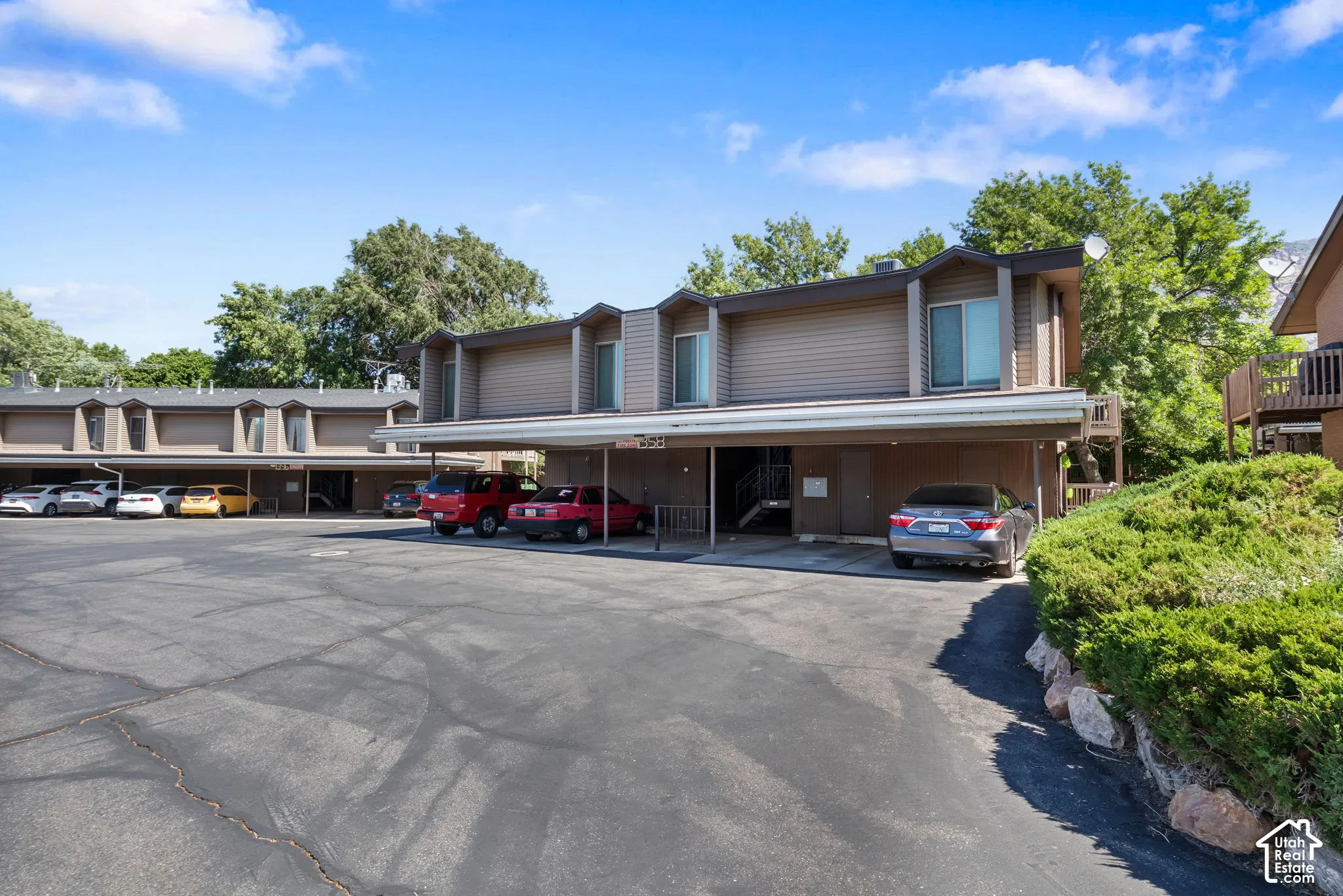 Multi-unit residential complex featuring covered parking spaces and a large paved lot
