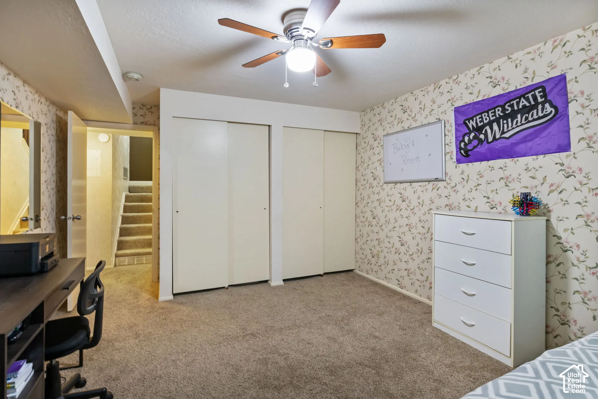 Carpeted room featuring a ceiling fan, dual sliding closet doors, and floral-patterned wallpaper