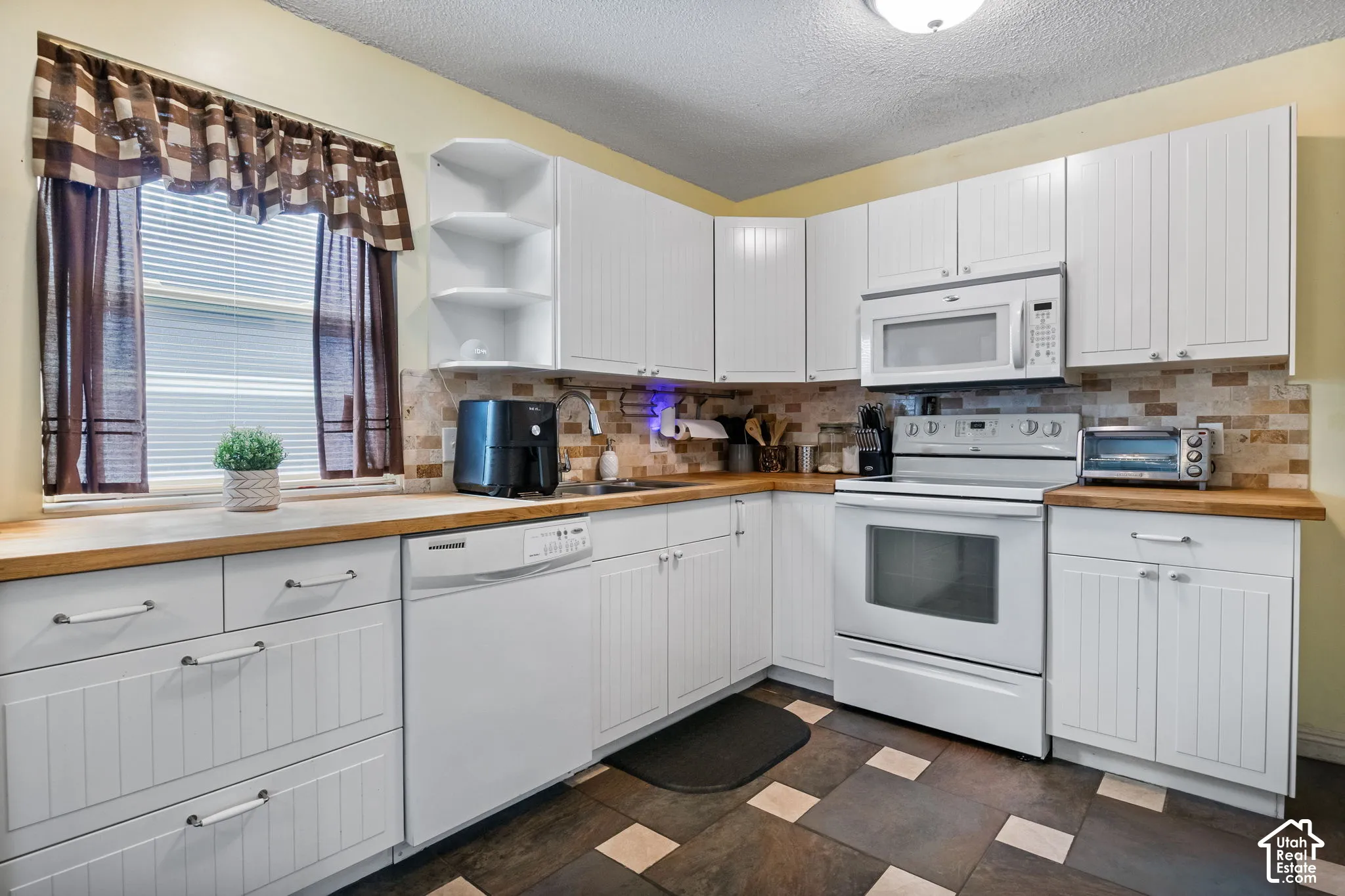Kitchen featuring white cabinetry with beadboard paneling, wood-finish countertops, and a tiled backsplash