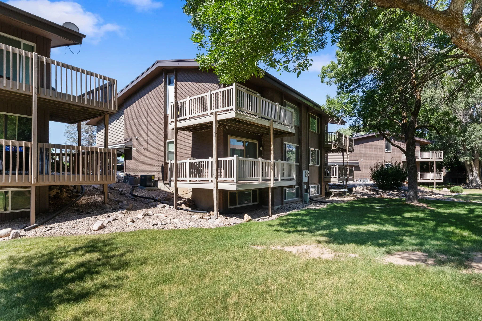 Multi-story building exterior featuring brown siding, multiple private balconies with wooden railings, and a manicured lawn area
