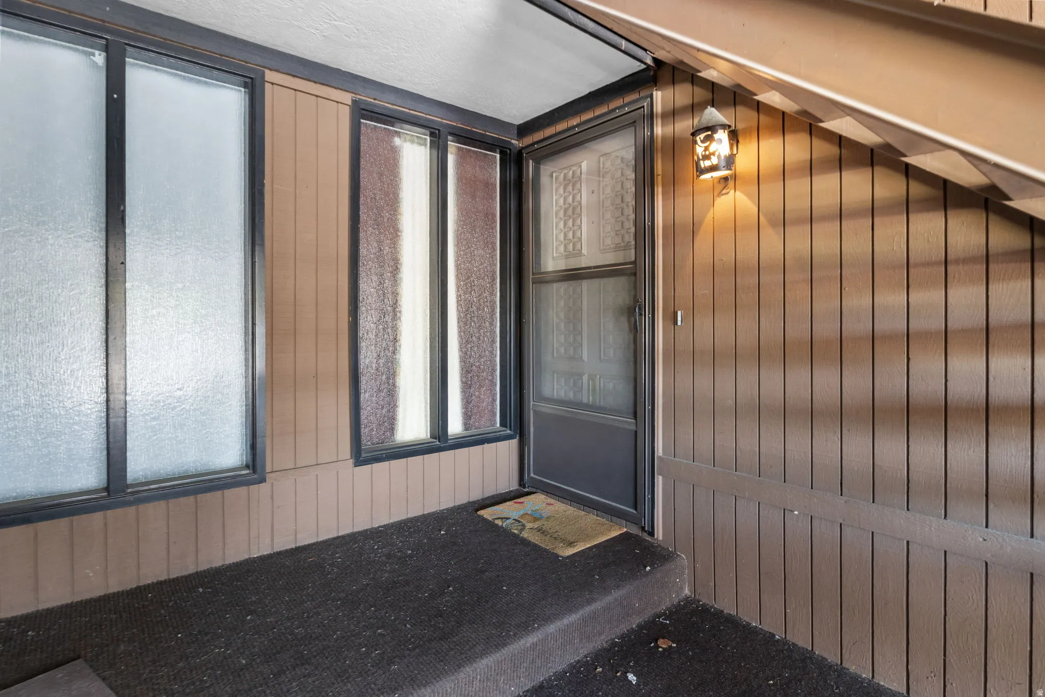 Covered entryway featuring vertical plank siding and a textured glass entry door