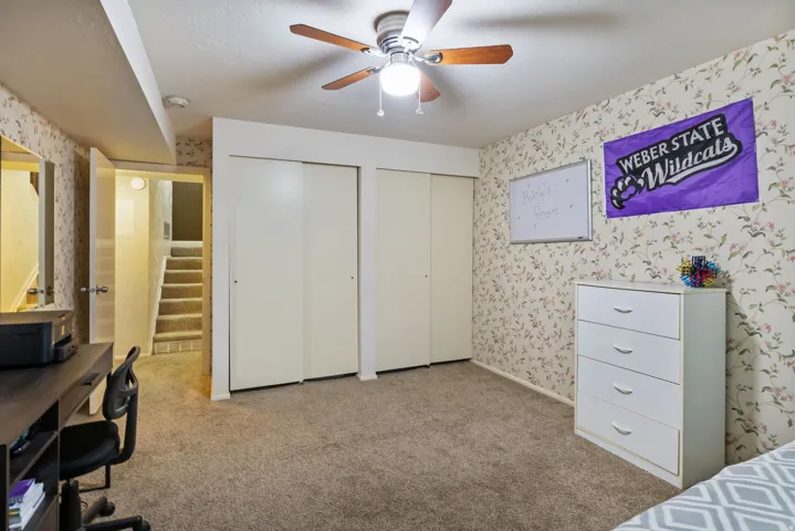 Carpeted room featuring a ceiling fan, dual sliding closet doors, and floral-patterned wallpaper