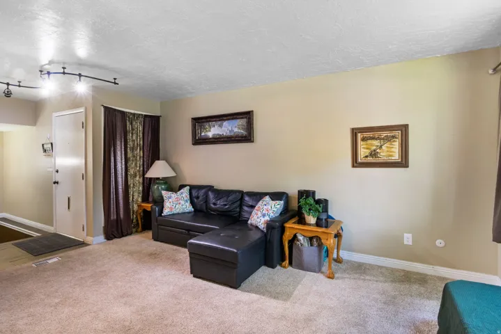 Carpeted living area featuring track lighting, a neutral wall color, and a white entry door with dark hardware