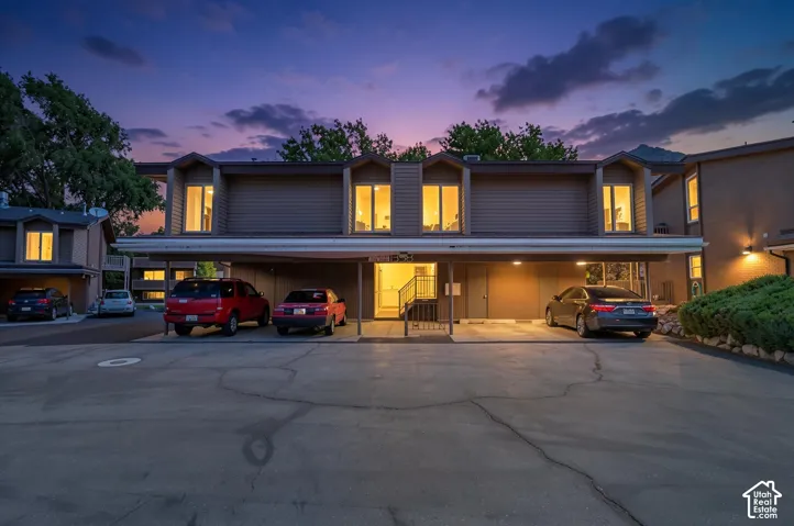 Multi-story residential building with carports below, featuring dormer windows and exterior lighting