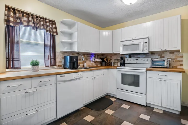Kitchen featuring white cabinetry with beadboard paneling, wood-finish countertops, and a tiled backsplash