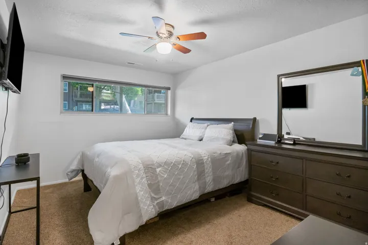 Carpeted room featuring a wide window, ceiling fan with light fixture, and white walls