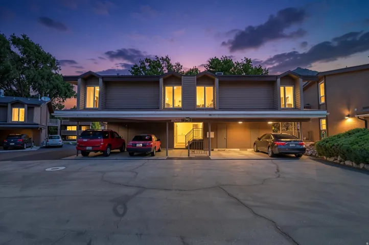 Multi-story residential building with carports below, featuring dormer windows and exterior lighting