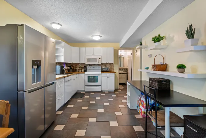 Kitchen featuring white cabinetry, wood-finish countertops, and a full suite of white appliances including a range, microwave, and dishwasher