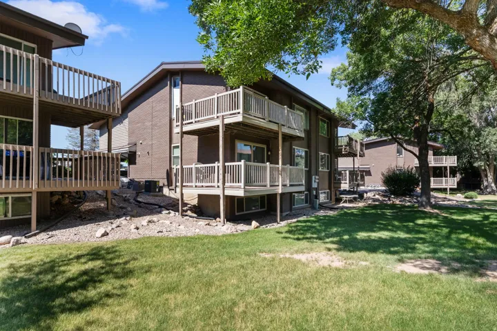 Multi-story building exterior featuring brown siding, multiple private balconies with wooden railings, and a manicured lawn area