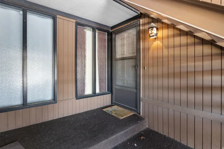 Covered entryway featuring vertical plank siding and a textured glass entry door