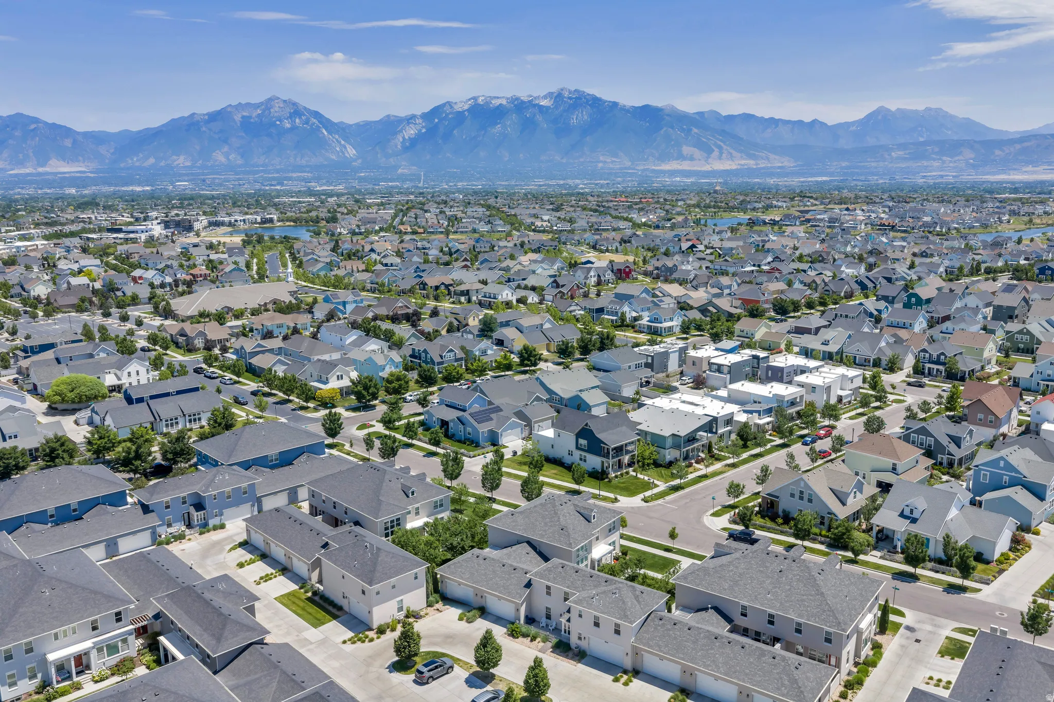 Expansive residential development with a variety of architectural styles, surrounded by manicured landscaping and mature trees, set against a backdrop of distant mountains