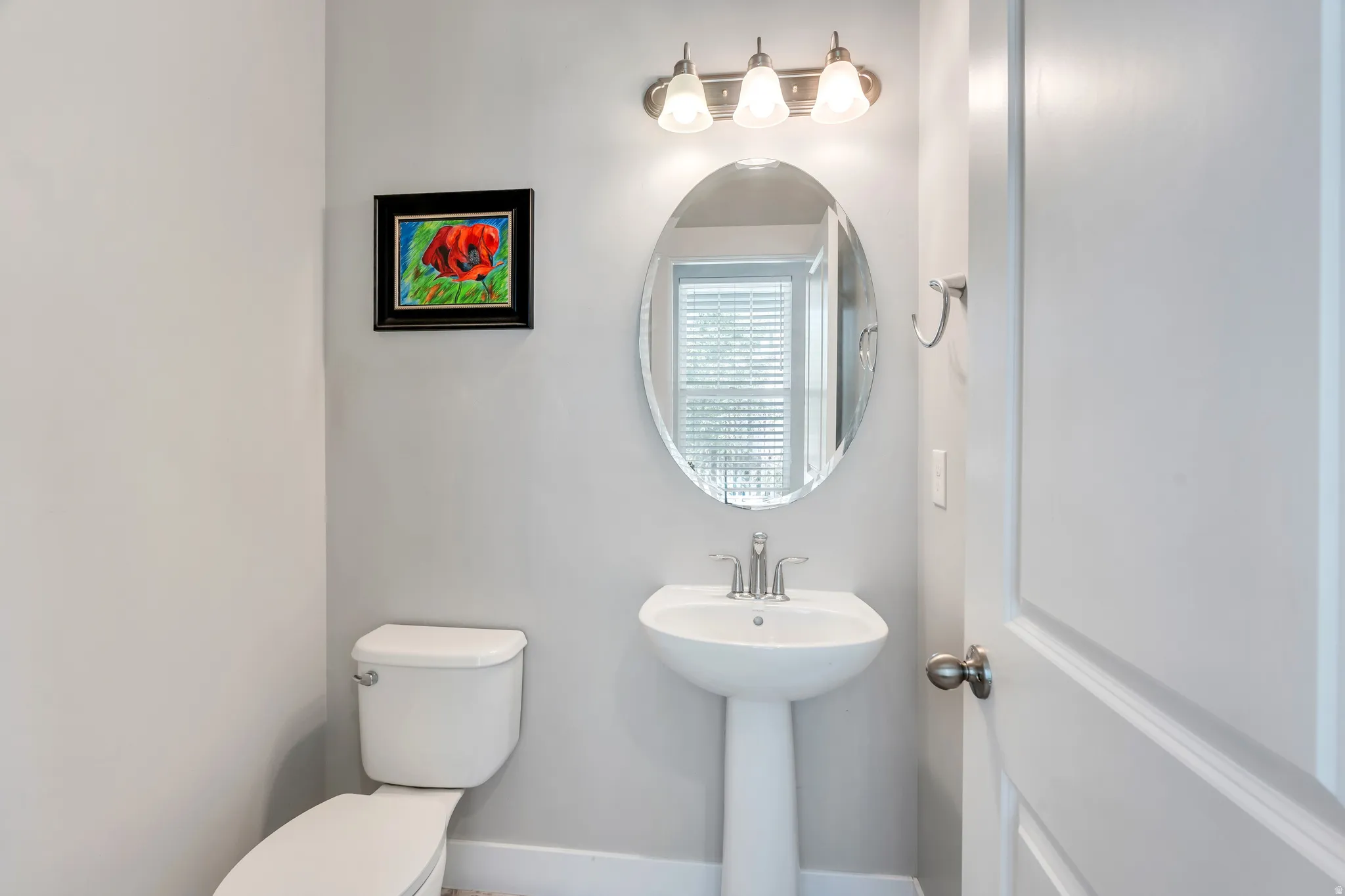 Pedestal sink with a polished chrome faucet, an oval mirror, and a three-light vanity fixture