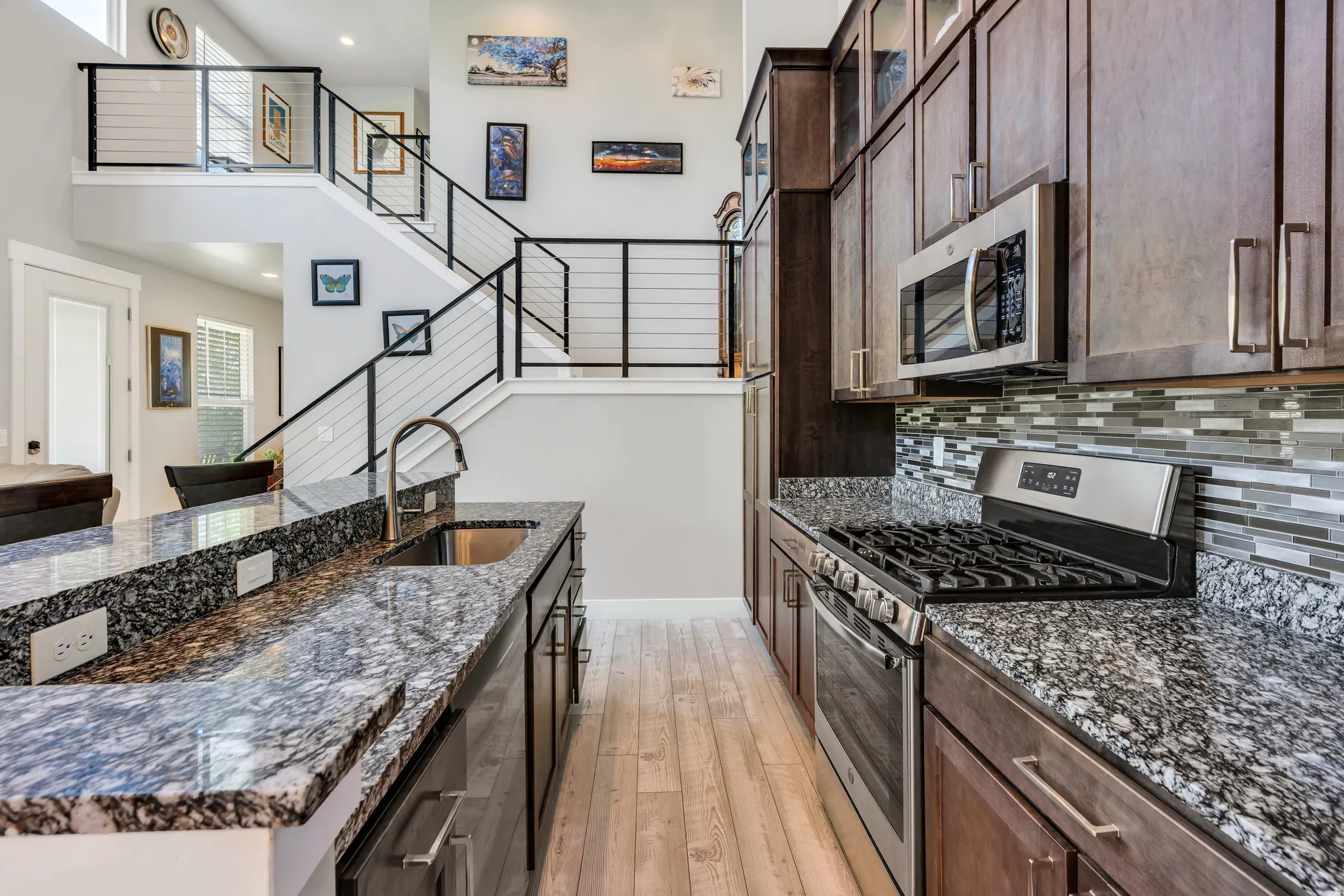 Kitchen featuring granite countertops, stainless steel appliances, wood-finish flooring, dark wood cabinetry, and a mosaic tile backsplash