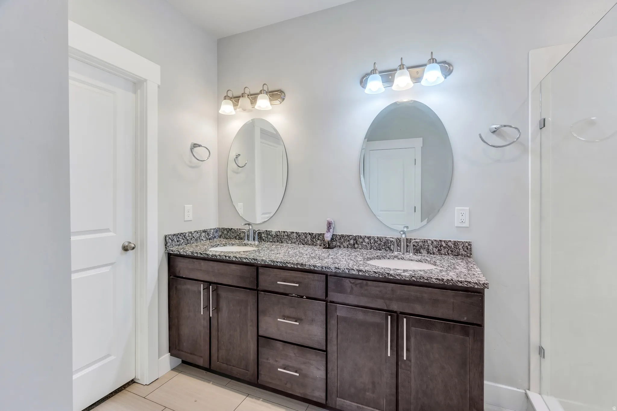 Double vanity featuring dark wood-finish cabinetry, speckled countertop, and two oval mirrors