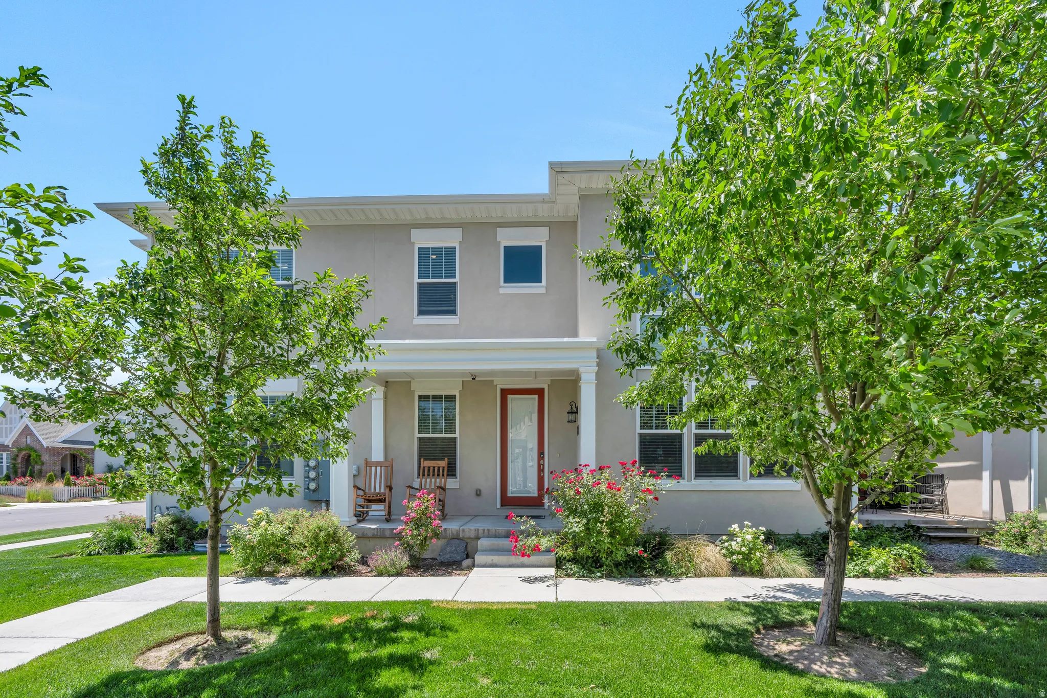 Two-story stucco residence featuring a covered front porch with white columns, a red entry door, and a manicured lawn with mature trees