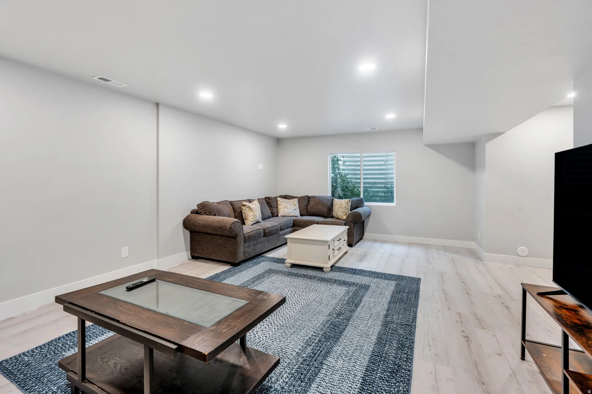 Spacious recreation room featuring light wood-finish flooring, recessed lighting, and a window with horizontal blinds