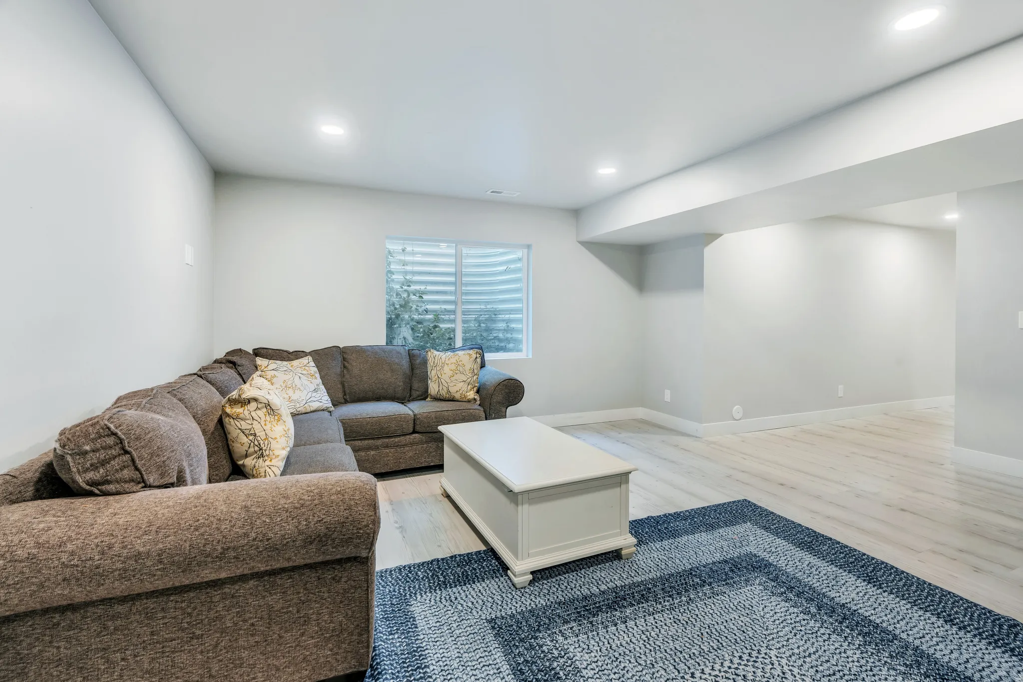 Spacious room featuring light wood-finish flooring, recessed lighting, a window with a window well, and neutral wall tones