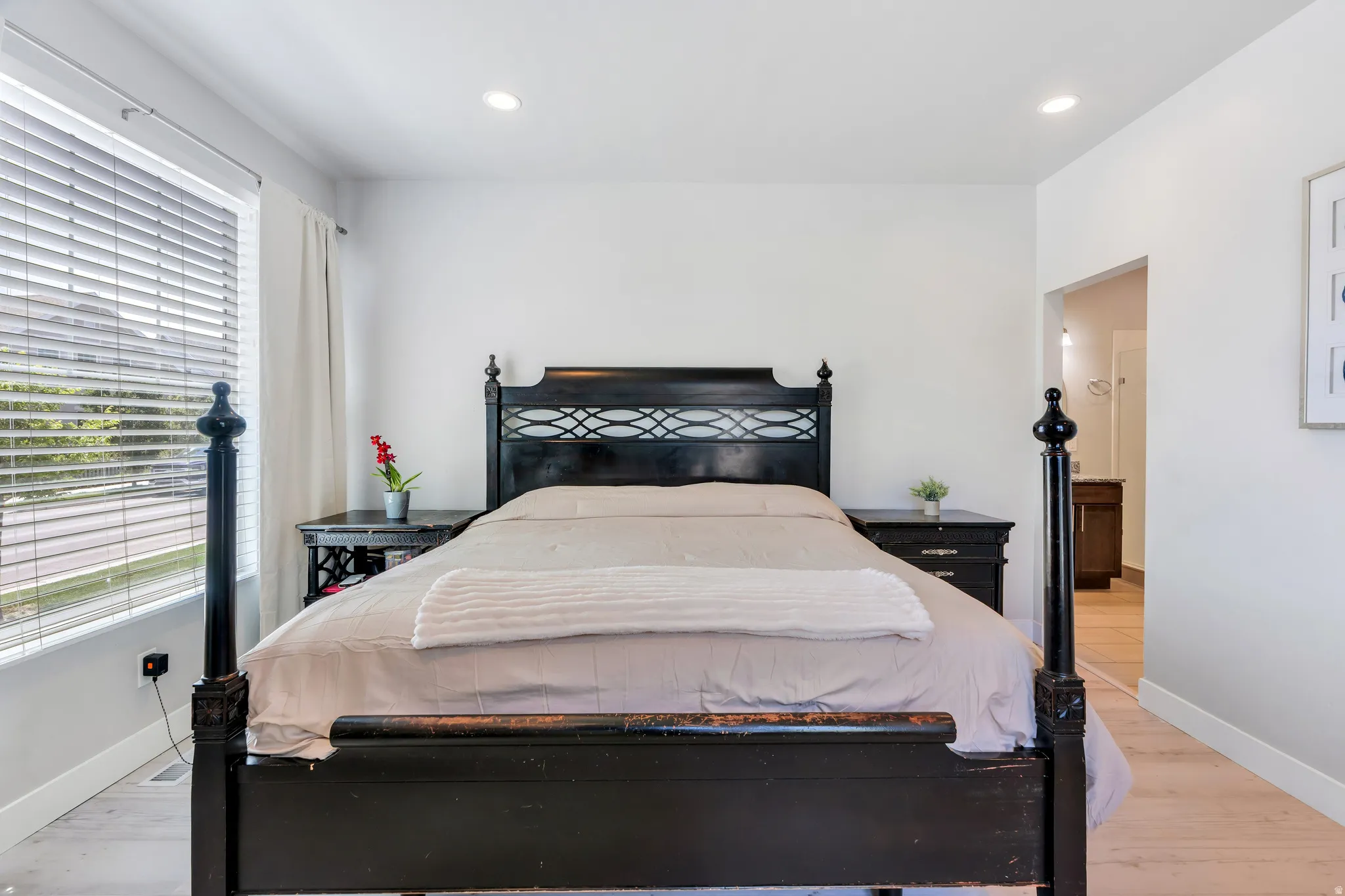 Bright bedroom featuring a large window with blinds, recessed lighting, light wood-finish flooring, and white walls