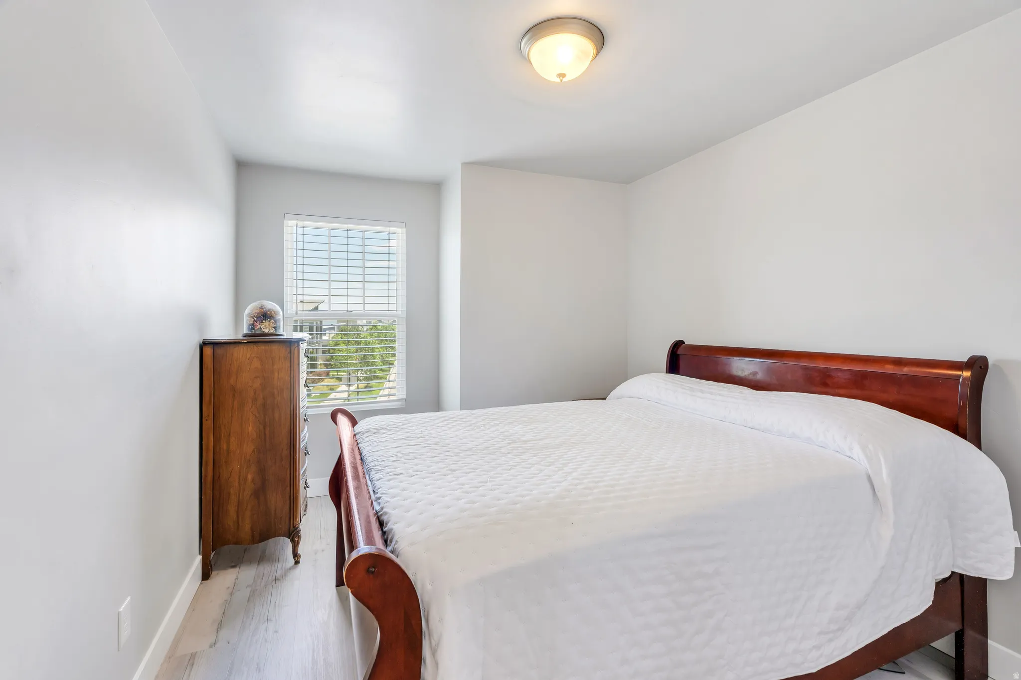 Bedroom featuring light wood-finish flooring, a window with horizontal blinds, and a flush-mount ceiling light fixture