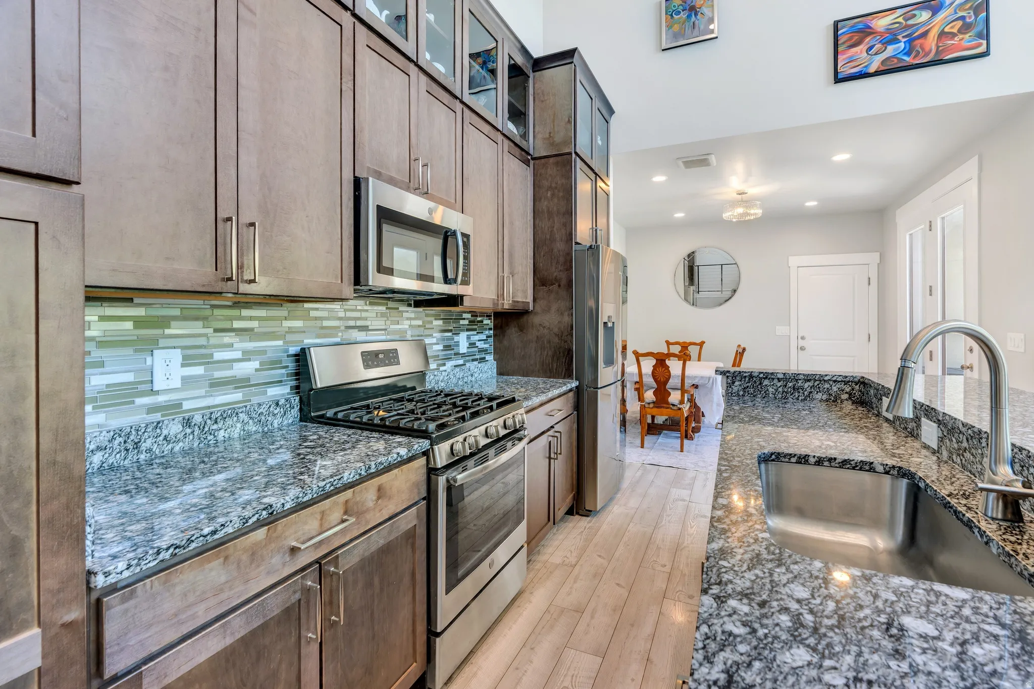 Kitchen featuring granite countertops, stainless steel appliances, wood-finish cabinetry, a glass tile backsplash, and a stainless steel sink with a gooseneck faucet
