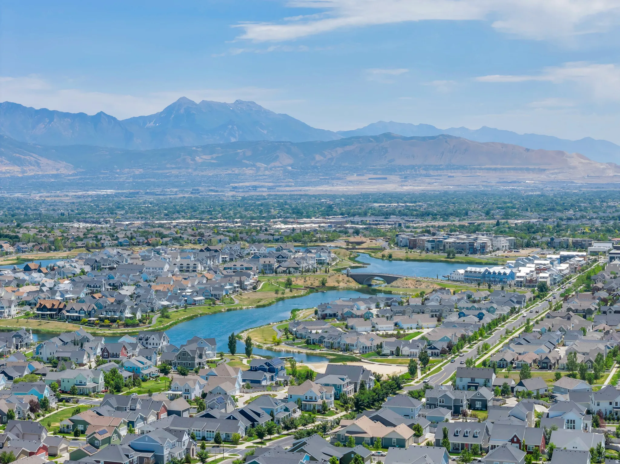 Expansive aerial showcasing a residential community with a large body of water, extensive green spaces, and a mountainous backdrop