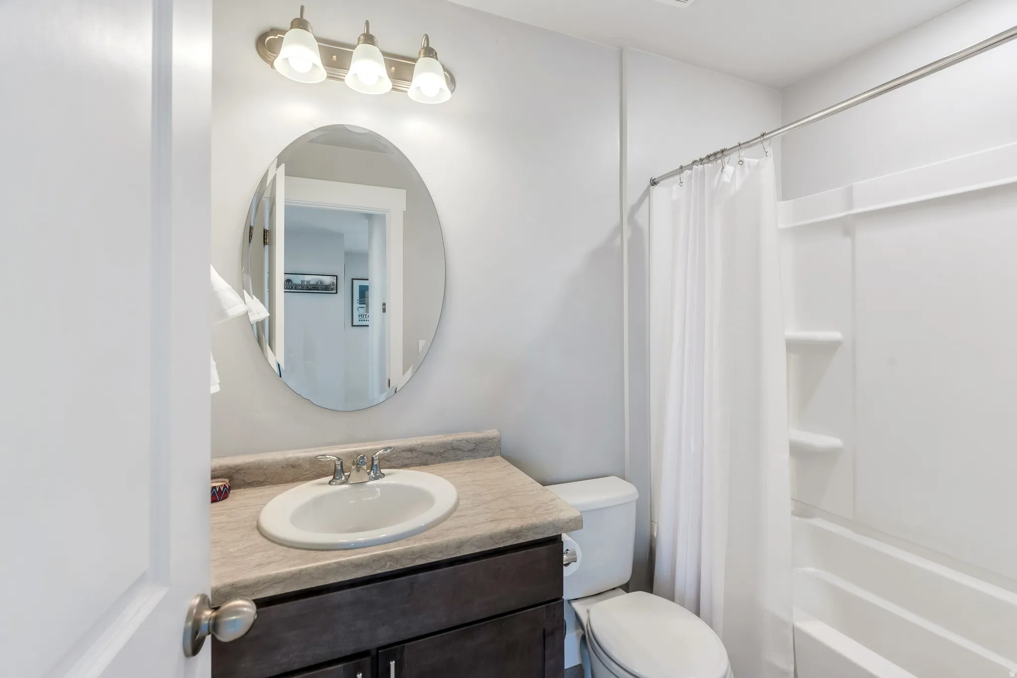 Full bathroom featuring a dark wood-finish vanity with an oval sink and a light-colored countertop, an oval wall mirror, and a shower-tub combination with built-in shelving