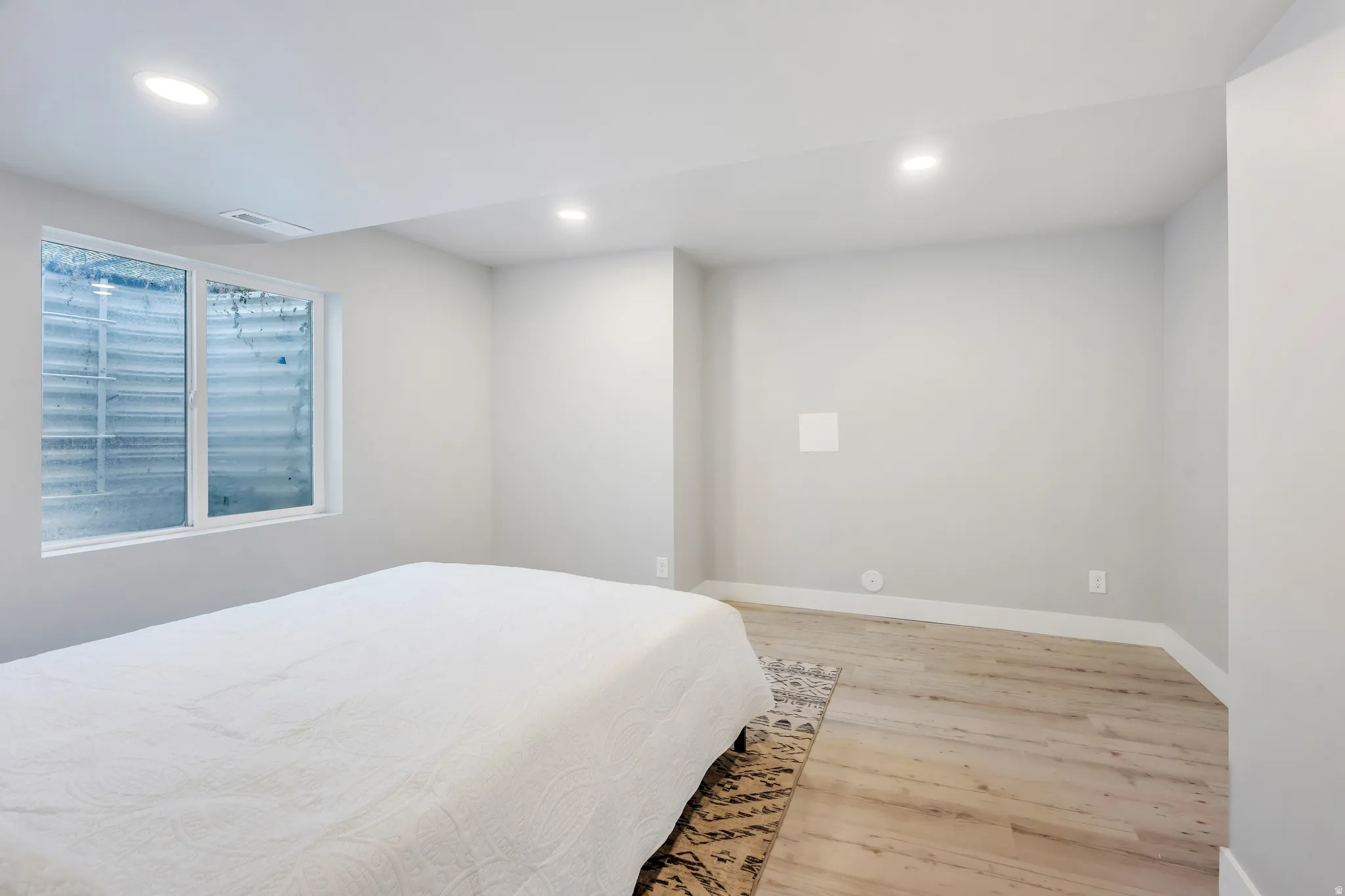 Spacious room featuring light wood-finish flooring, recessed lighting, and a large egress window