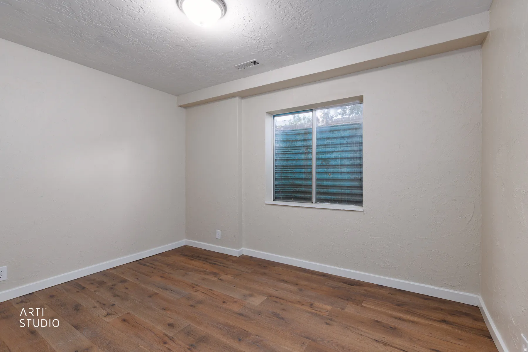 Room featuring wood-finish flooring, light neutral wall tones, white baseboards, and a window with a textured screen