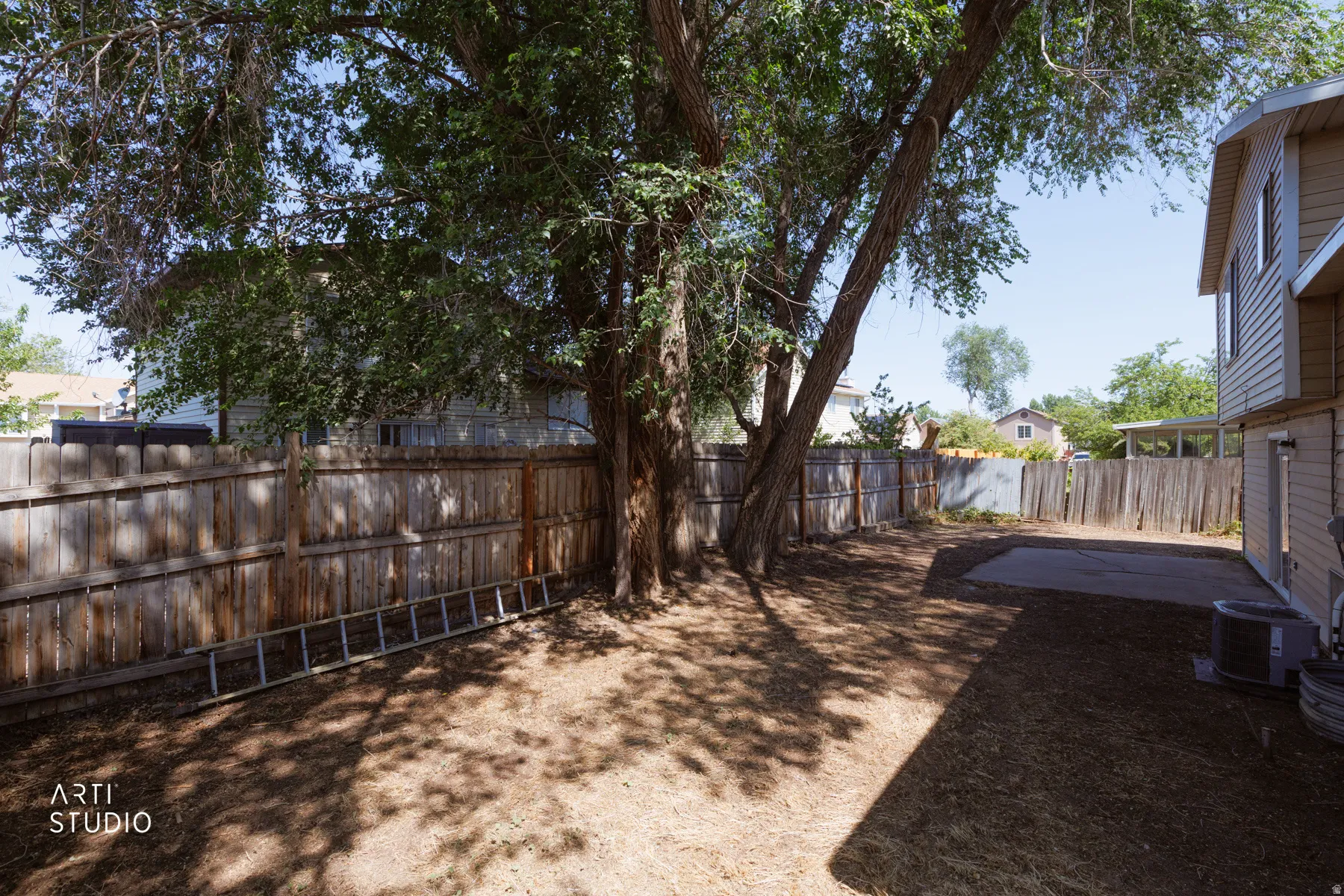 Fenced backyard featuring mature shade trees, a concrete patio, and a light-colored siding exterior