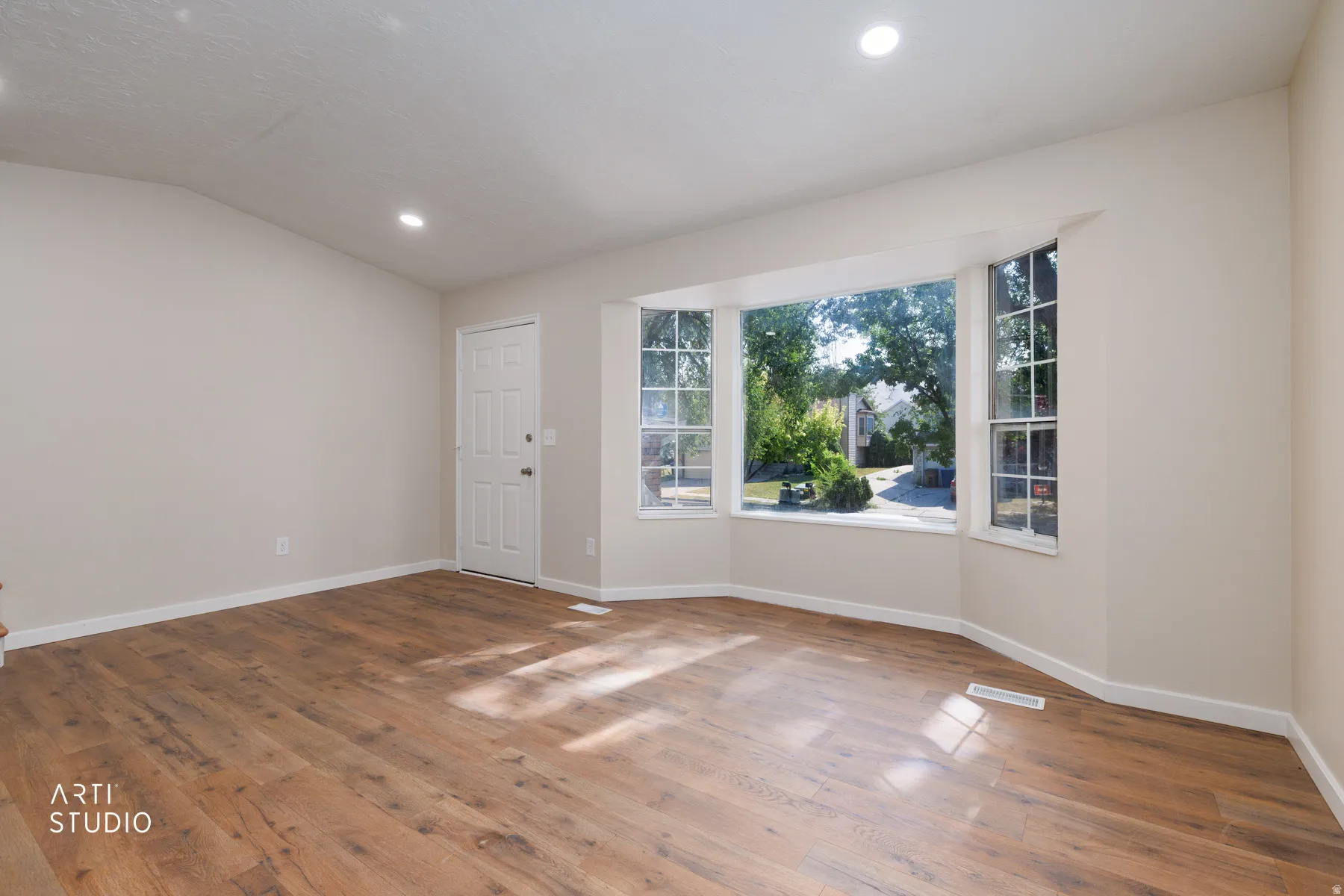 Bright living space featuring a bay window with multiple panes, wood-finish flooring, recessed lighting, and a paneled entry door