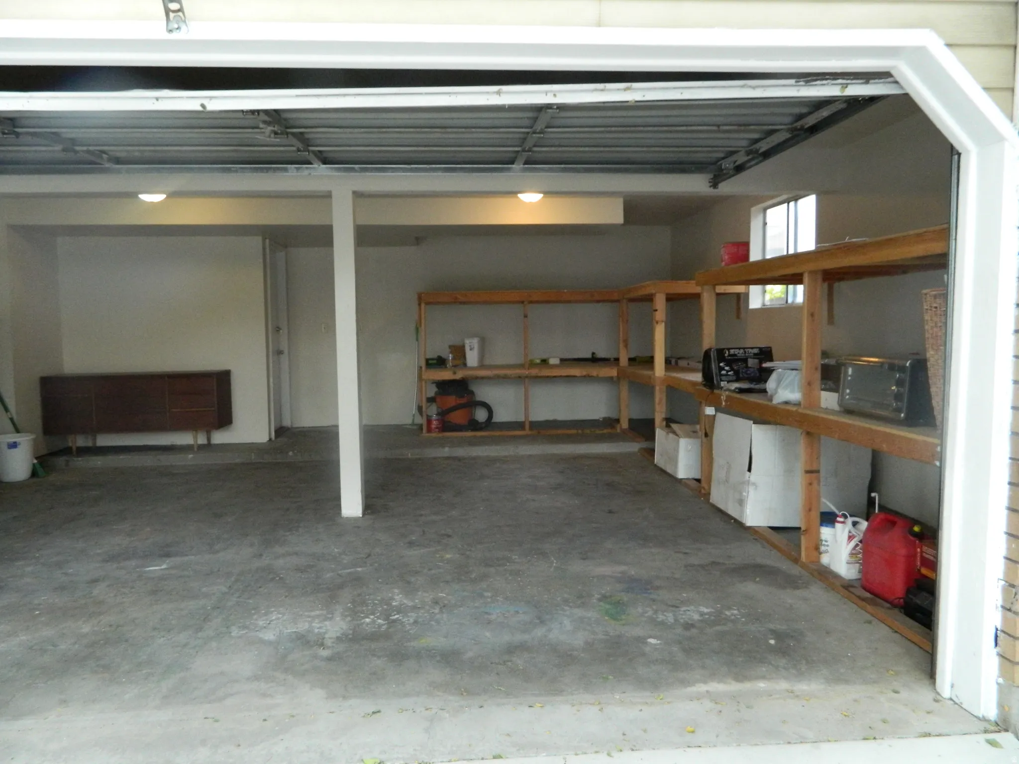 Spacious garage featuring a concrete floor, built-in wooden shelving, overhead lighting, and a single window