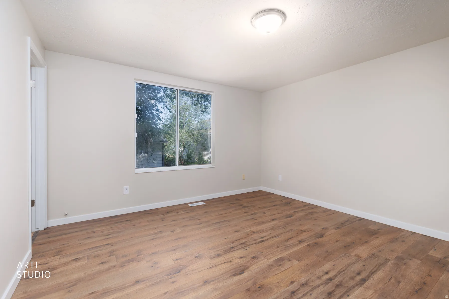 Spacious room featuring wood-finish flooring, white baseboards, and neutral wall paint