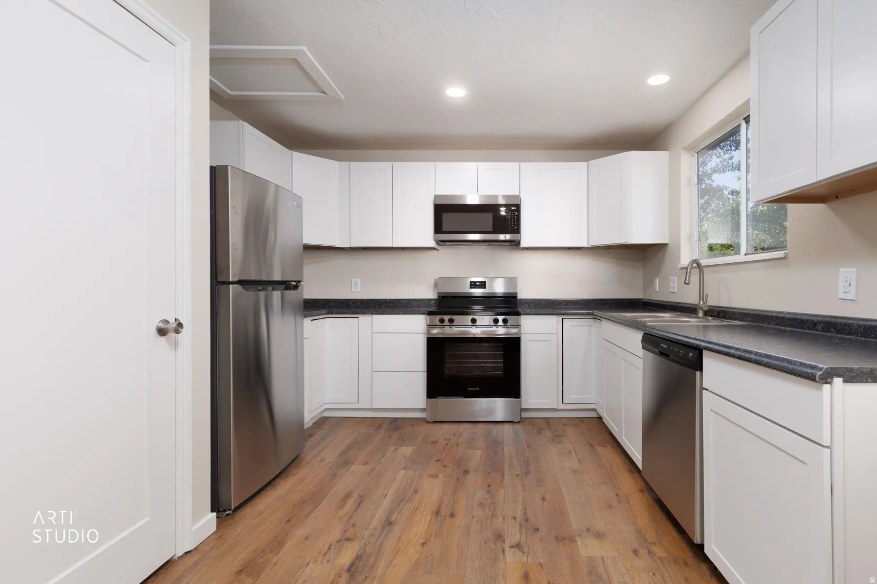 Modern kitchen featuring white cabinetry, dark countertops, and wood-finish flooring