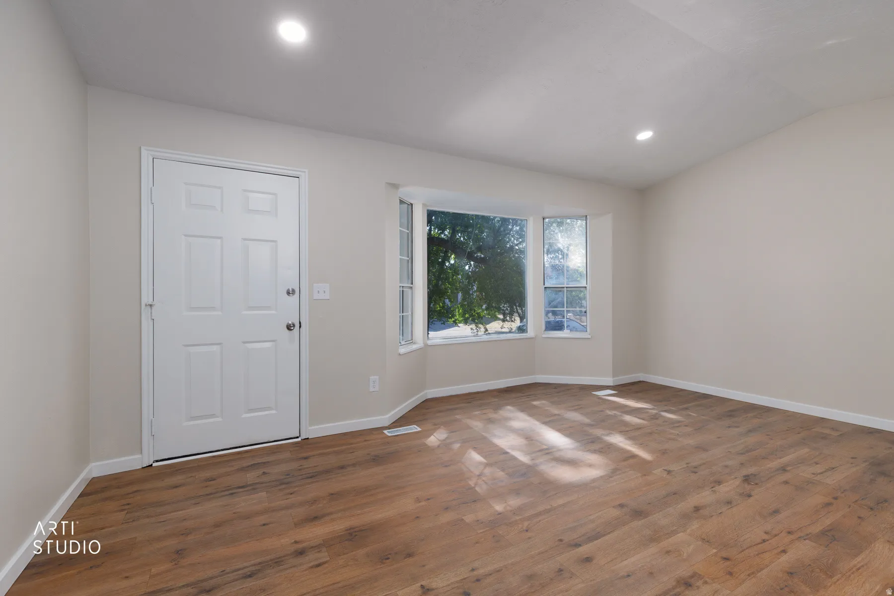 Spacious room with wood-finish flooring, recessed lighting, and a multi-panel bay window
