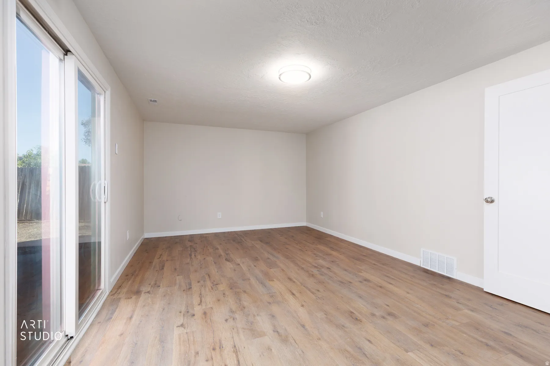 Spacious room with wood-finish flooring and a white sliding glass door