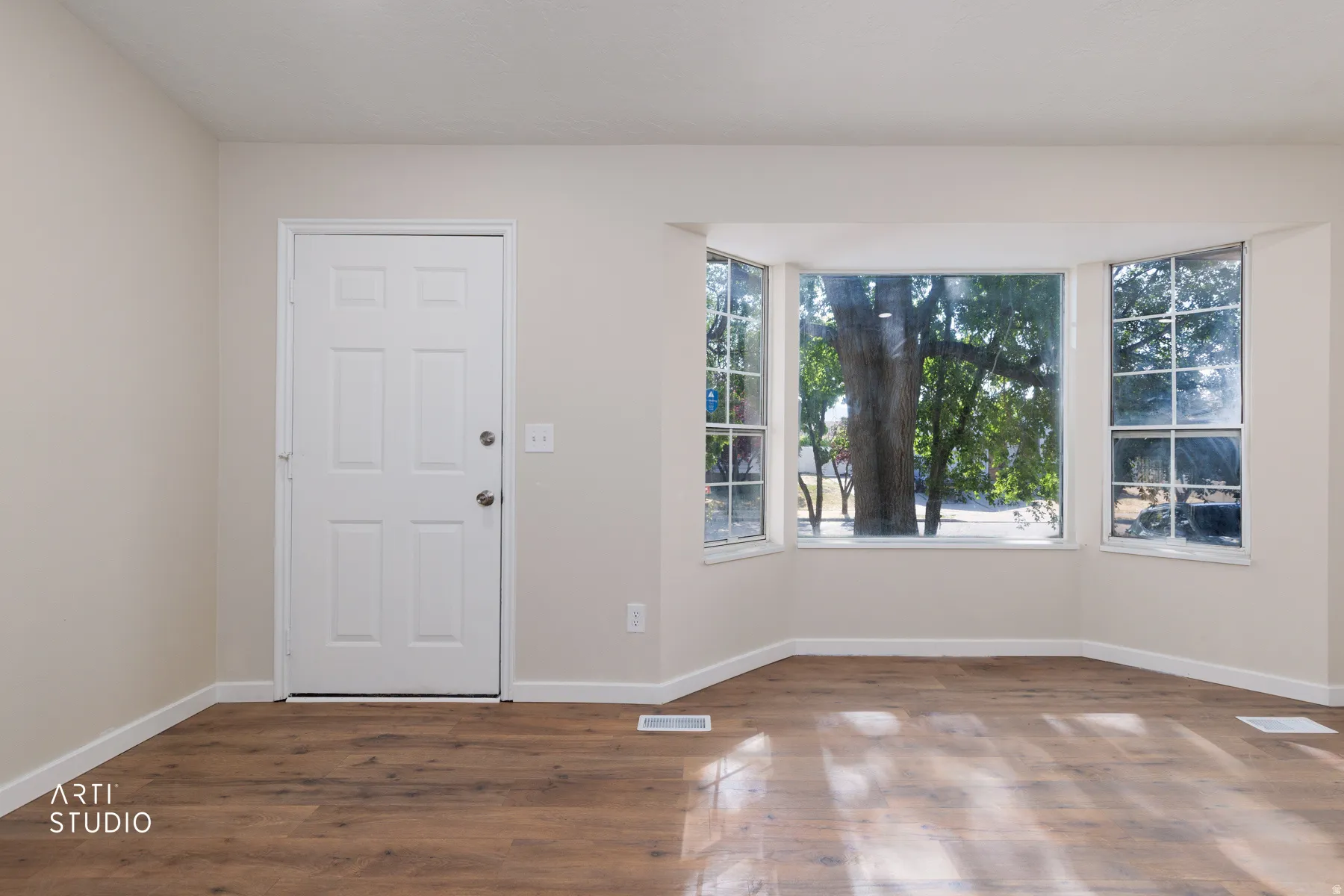 Living space featuring new Pergo laminate finish flooring, a white six-panel entry door, and a bay window with multiple panes