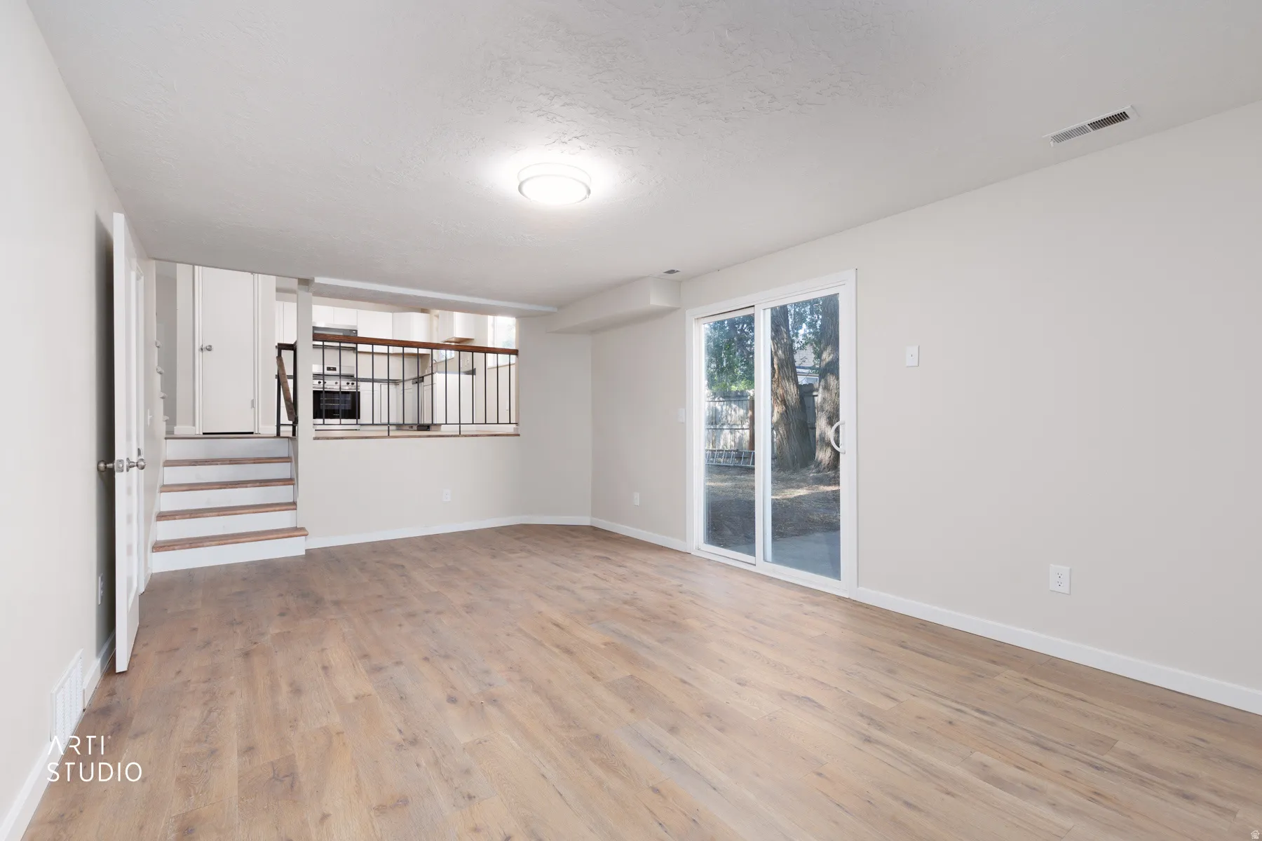 Spacious living area featuring wood-finish flooring, light-toned walls, and a sliding glass door
