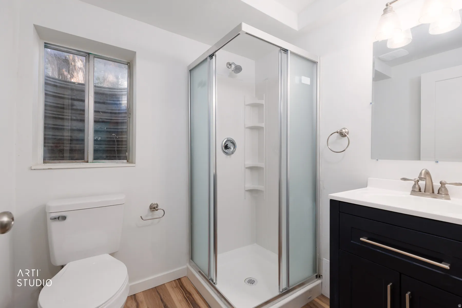 Basement Modern bathroom featuring a corner shower enclosure with frosted glass, a dark wood-finish vanity with a white countertop and integrated sink, brushed nickel fixtures, and wood-finish flooring