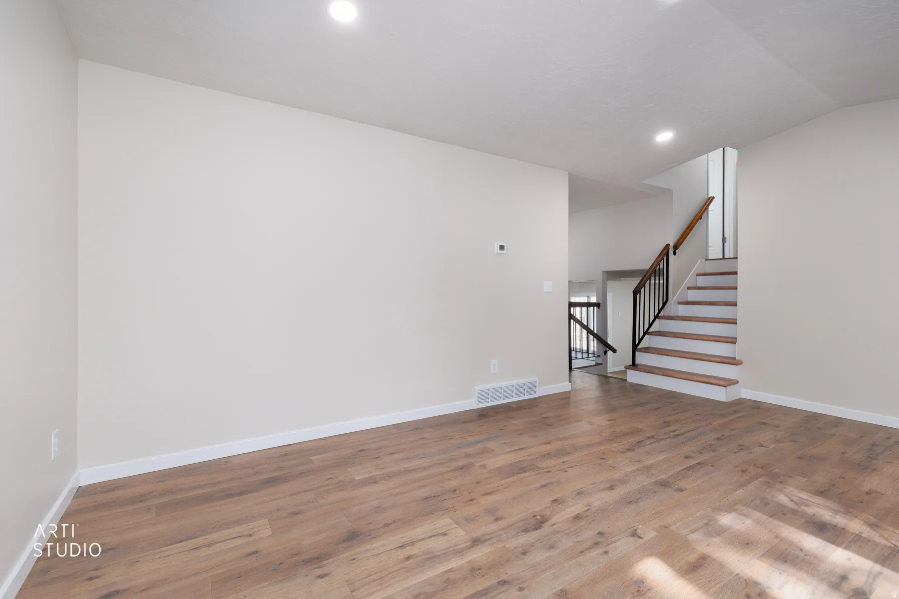 Open living area featuring wood-finish flooring, recessed lighting, and a contemporary staircase with dark balusters and a wood handrail