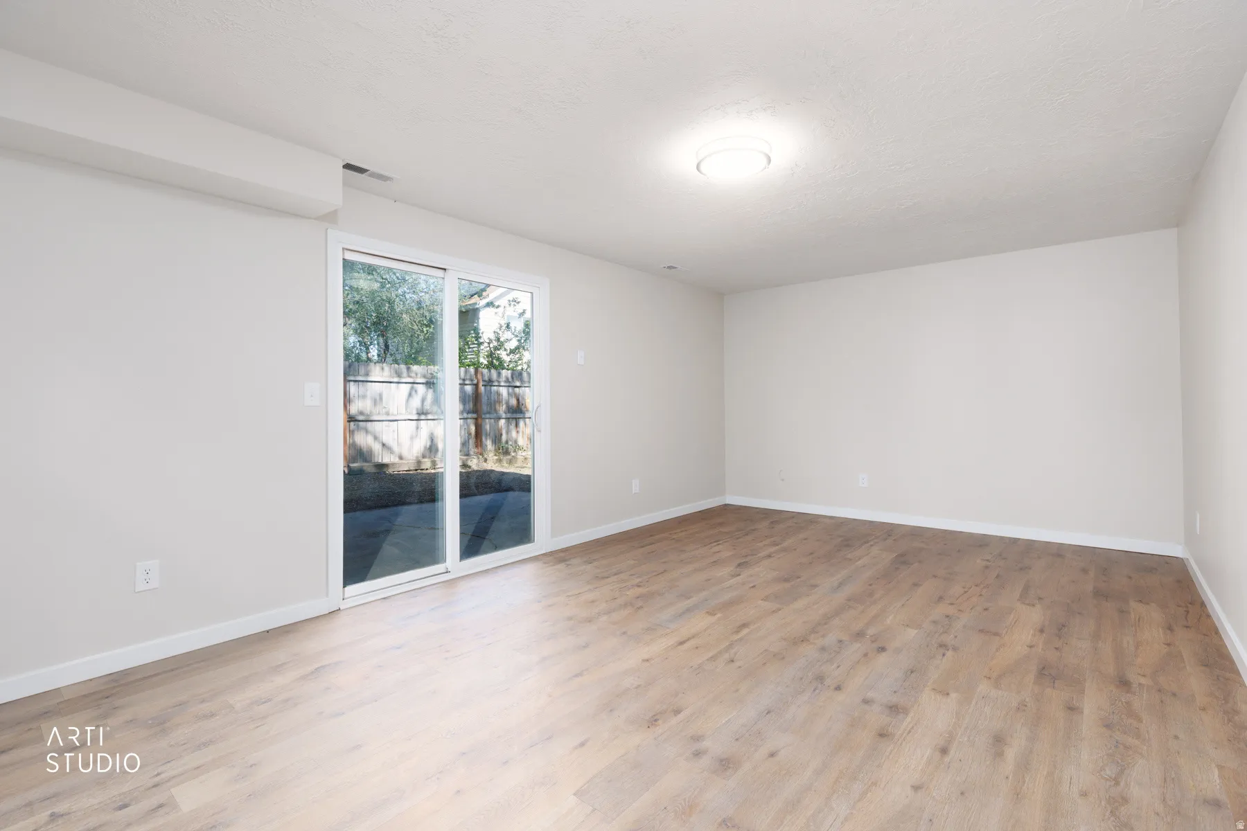 Spacious room featuring wood-finish flooring, light-toned walls, and a ceiling-mounted light fixture