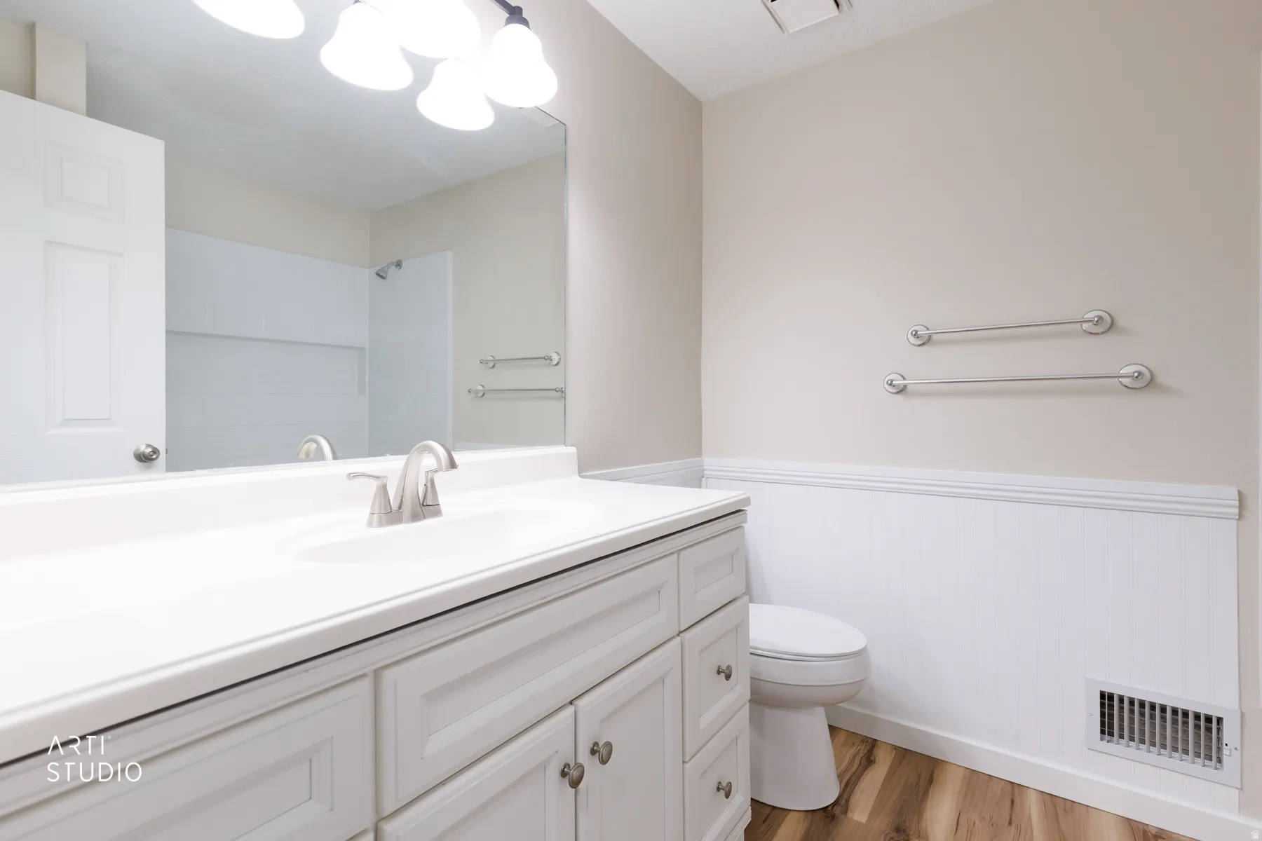 Bathroom featuring a single vanity with a white countertop and brushed nickel faucet, a large wall-mounted mirror, overhead vanity lighting, and wood-finish flooring