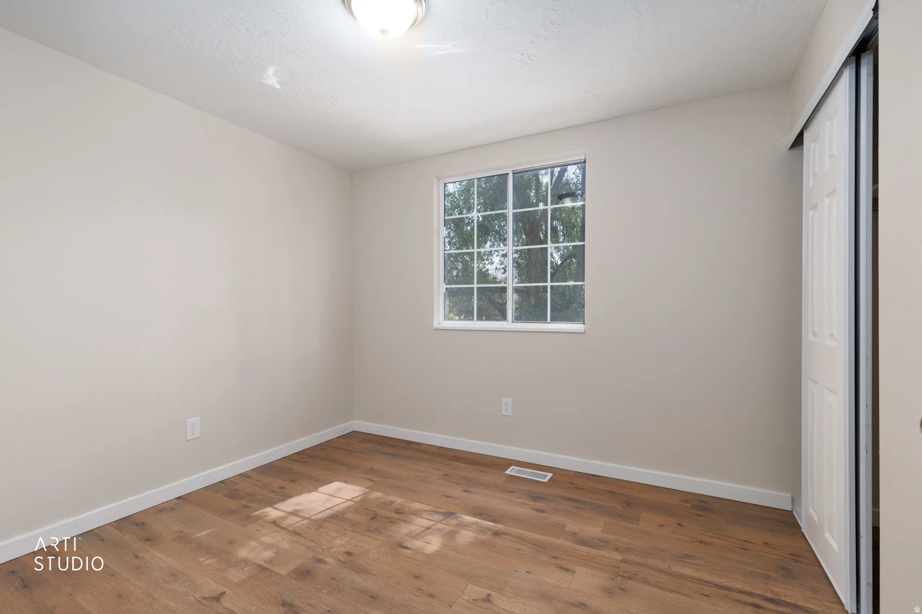 Neutral-toned interior with wood-finish flooring, a window offering natural light, white baseboards, and a sliding closet door