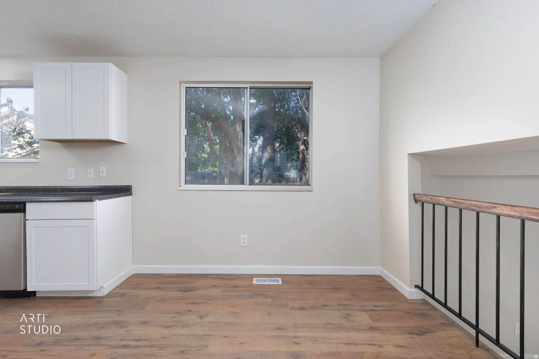 Open concept area featuring wood-finish flooring, white cabinetry, dark countertops, a stainless steel dishwasher, and a metal baluster railing with a wood handrail