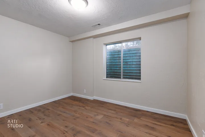 Room featuring wood-finish flooring, light neutral wall tones, white baseboards, and a window with a textured screen