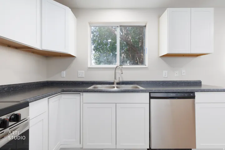 Kitchen featuring white shaker-style cabinetry, dark countertops, a double basin stainless steel sink with a brushed nickel faucet, and a stainless steel dishwasher