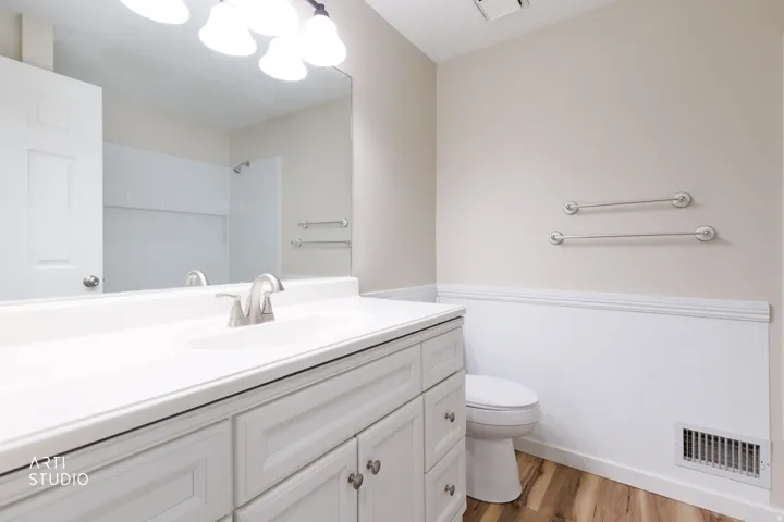 Bathroom featuring a single vanity with a white countertop and brushed nickel faucet, a large wall-mounted mirror, overhead vanity lighting, and wood-finish flooring