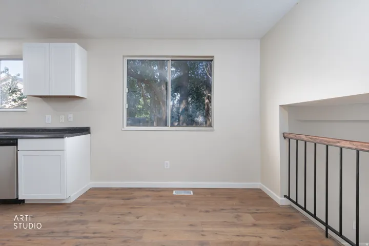 Open concept area featuring wood-finish flooring, white cabinetry, dark countertops, a stainless steel dishwasher, and a metal baluster railing with a wood handrail